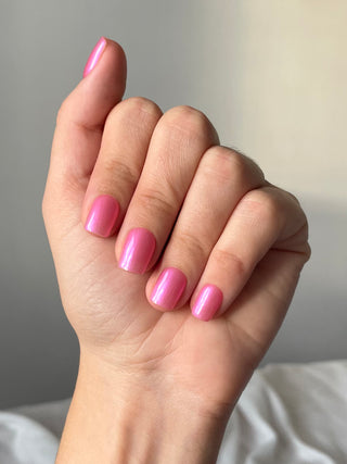 Les ongles de la main portent des press on nails du modèle court rose irisé.